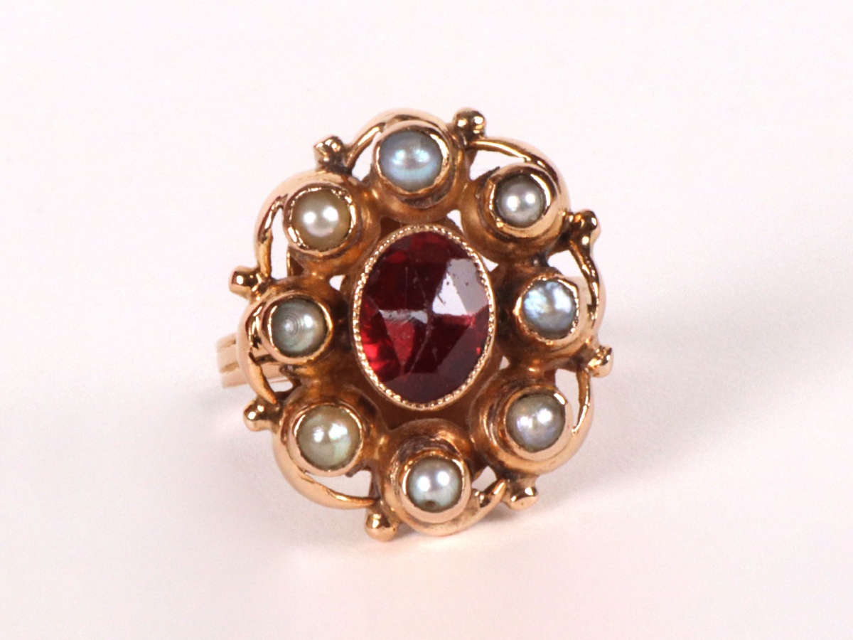 Old ring in yellow gold in the shape of a daisy including an oval shaped orange colored tourmaline stone surrounded by 8 small pearls