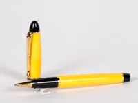 قلم روللر Aurora Ipsilon، SKU IB02835، من ريزين أصفر مع زخرفة ذهبية وغطاء أسود، على خلفية بيضاء.