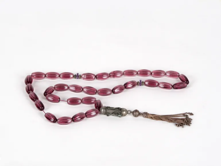 IB03635 chapelet masbaha en verre couleur améthyste, perles ovales et pendant en cuivre sur fond blanc.