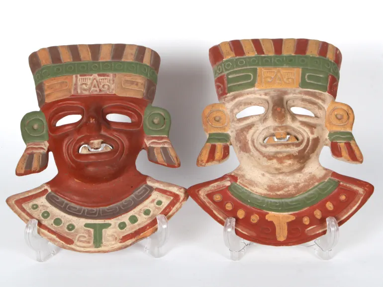 Two painted terracotta masks, IB04480, with Aztec-style faces in red, cream, green and ochre on stands.