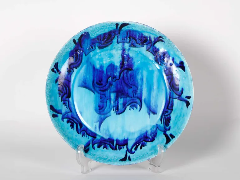 IB06036 Plat en céramique bleue glaçurée à décor abstrait bleu foncé, présenté sur un support.