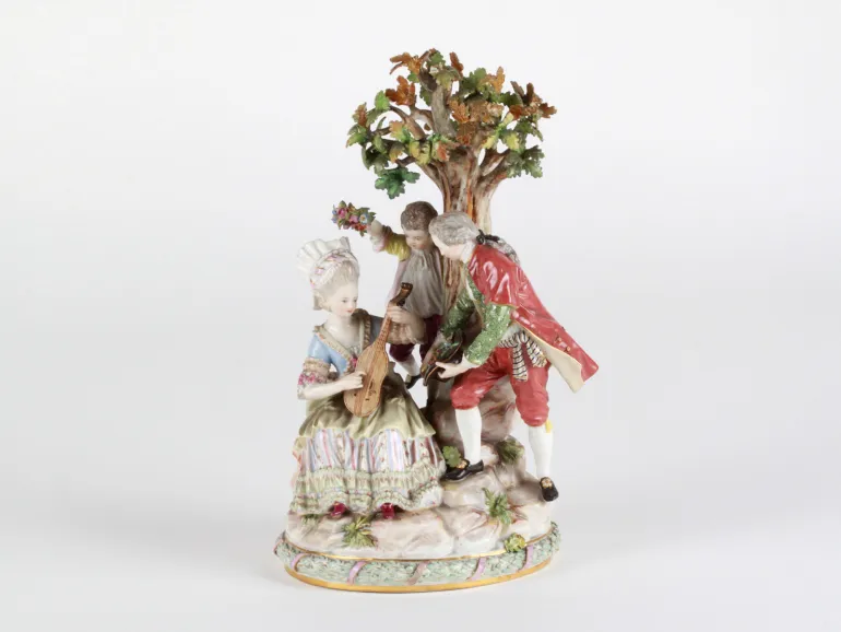 Groupe en porcelaine Meissen IB08062 : une femme à la mandoline, un gentilhomme offrant des fleurs et un enfant tenant une couronne de roses sous un arbre.