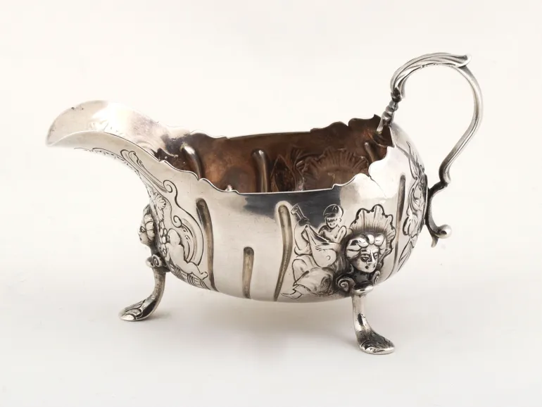 Sterling silver sauceboat with one handle and three feet, decorated with figures and scrollwork, SKU IB09116.