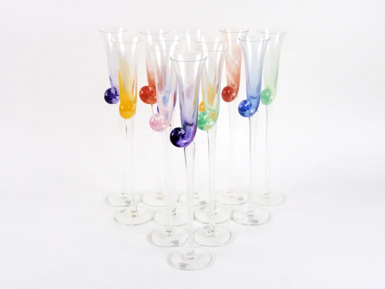 IB09130 : dix flûtes à champagne en verre soufflé coloré, signées Elena, avec décor en colimaçon, présentées groupées sur fond blanc.