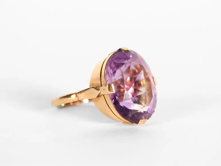 Gold ring featuring a large faceted purple gemstone, viewed from the side.