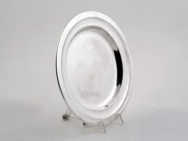 SKU IB00220 : plat rond en métal argenté Beard, présenté debout sur un support transparent.