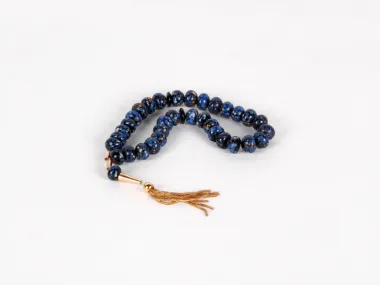 IB03652: antique Masbaha rosary with spotted blue glass beads and a gold pendant tassel on a white background.