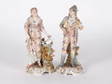 SKU IB04438: Two late 19th-century German porcelain sculptures of a young man and woman in traditional costumes, richly painted, standing by a fountain.