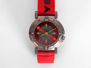Round watch with red face, green and orange hands, red strap, and bronze case.