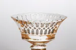 IB02447 كأس صغيرة من الخَزَف المُخرَّم على شكل زورق بقاعدة، أبيض ومذهَّب، على خلفية بسيطة.