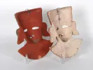 Two painted terracotta masks, red and beige, displayed on stands, SKU IB04480.