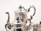 طقم شاي وود اند هيوغز من الفضة الإسترليني، SKU IB04739، يظهر إبريق شاي ووعاء بغطاء ووعاء مزخرفة بنقوش نباتية وغطاءات بقبضة على شكل بلوطة.
