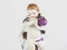 تمثال Meissen Porcelain رقم IB08071 لطفل يرتدي معطفًا مبطنًا بالفرو ويحمل كرة بنفسجية، على خلفية بيضاء.