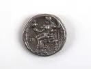 IB08962 tetradrachme grec en argent d’Alexandre III, montrant une figure assise usée sur la pièce.