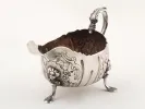 IB09116 18th-century Irish sterling silver sauceboat with one handle, ornate floral and figural decoration, and three feet.