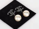 أقراط Chanel IB09231 على شكل CC مع لآلئ كبيرة متدلية، معروضة على وسادة سوداء.