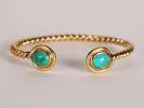 Gold twisted cuff bracelet featuring two turquoise stones on either side.